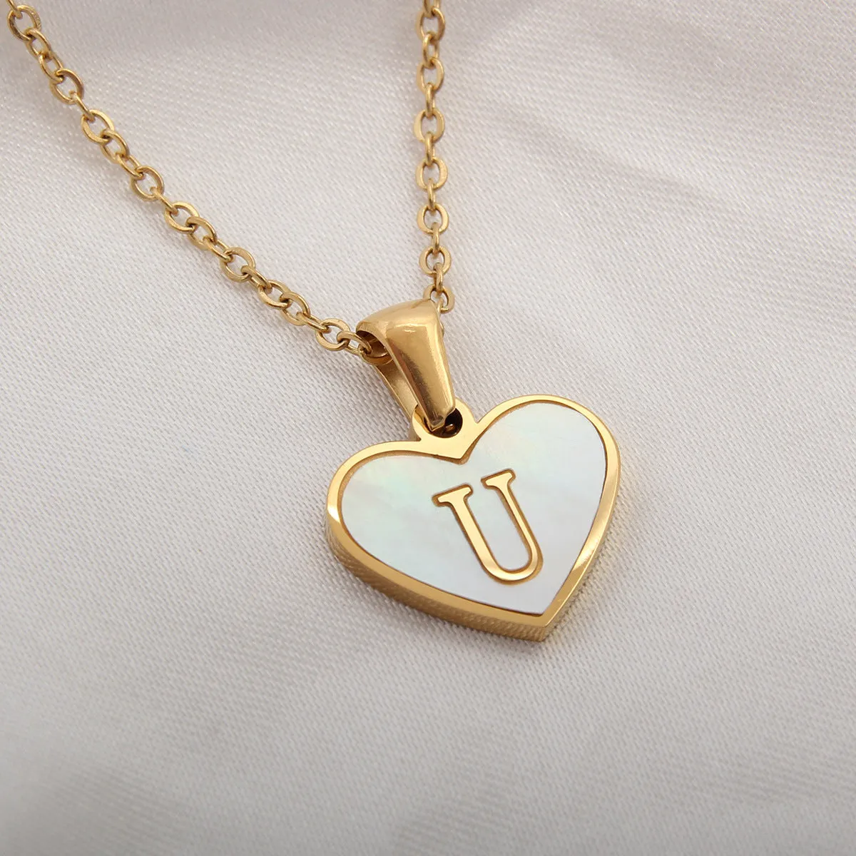 Gold-plated heart-shaped white shell initial necklace on a model, showing the adjustable clavicle chain.