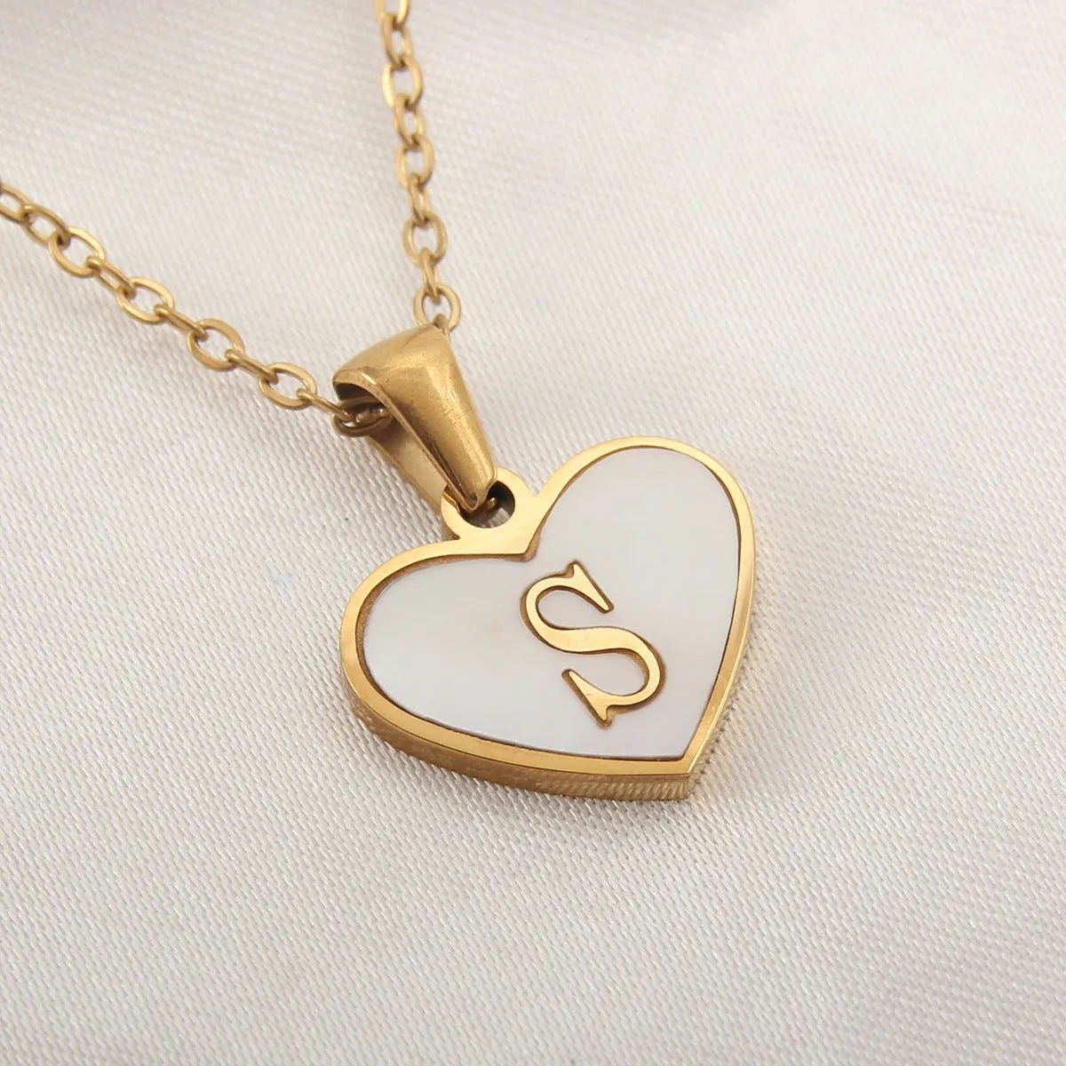 Gold-plated heart-shaped white shell initial necklace on a model, showing the adjustable clavicle chain.