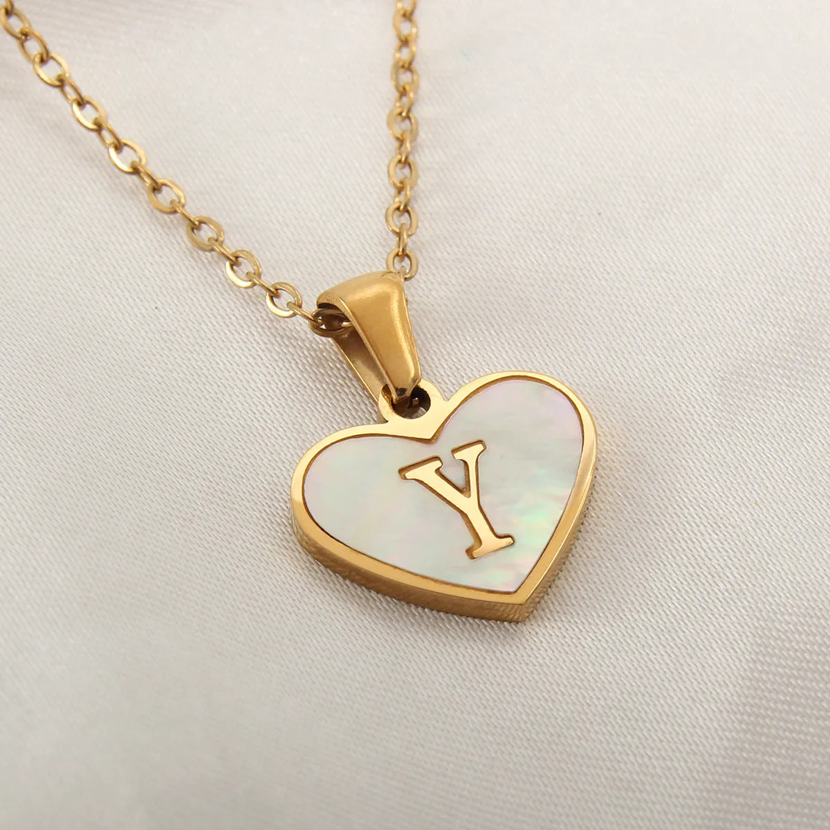 Gold-plated heart-shaped white shell initial necklace on a model, showing the adjustable clavicle chain.