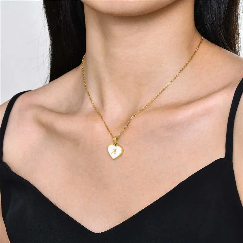 Gold-plated heart-shaped white shell initial necklace on a model, showing the adjustable clavicle chain.