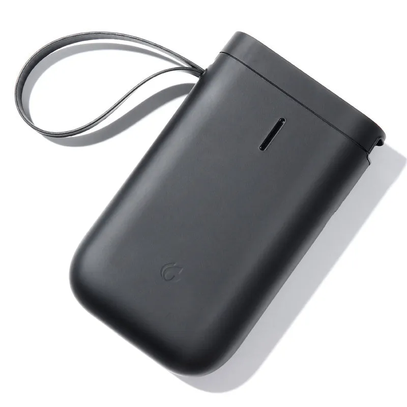 Compact black D11 Bluetooth thermal label printer on a desk next to a smartphone showing the label design app.