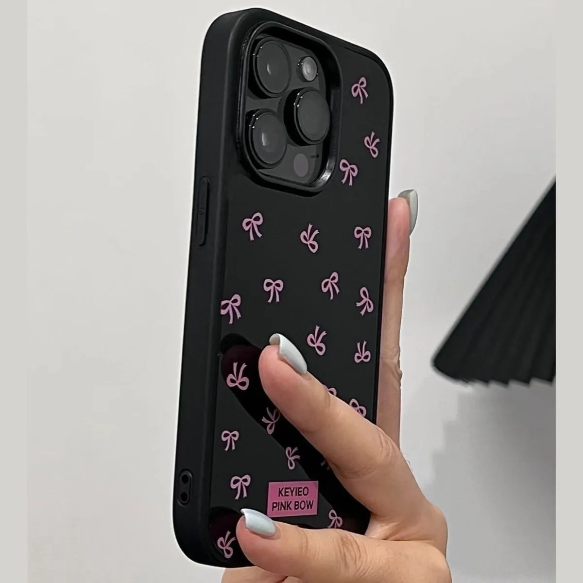 Black silicone iPhone case with sweet bow design placed on a white surface, all-inclusive back and side coverage