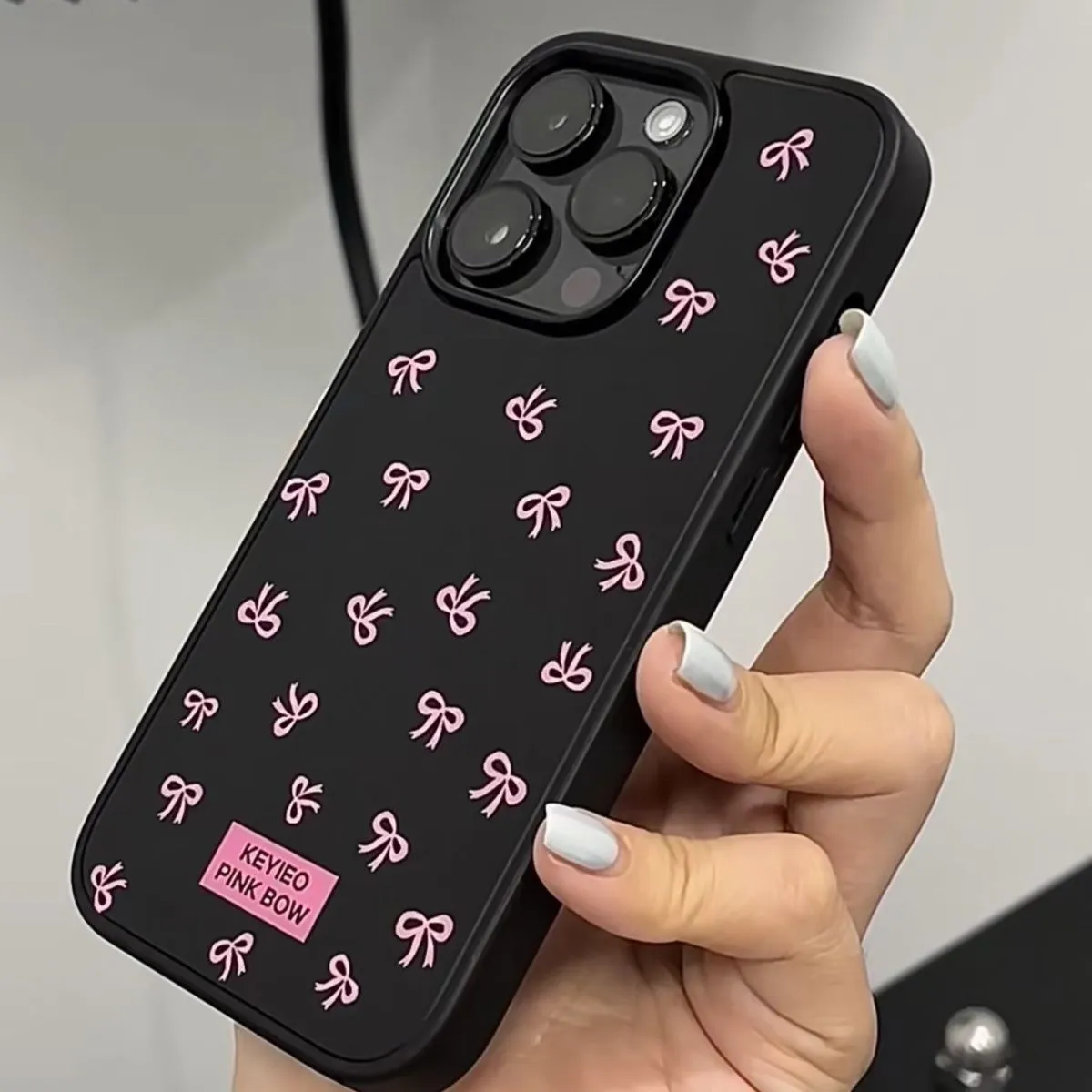 Black silicone iPhone case with sweet bow design placed on a white surface, all-inclusive back and side coverage