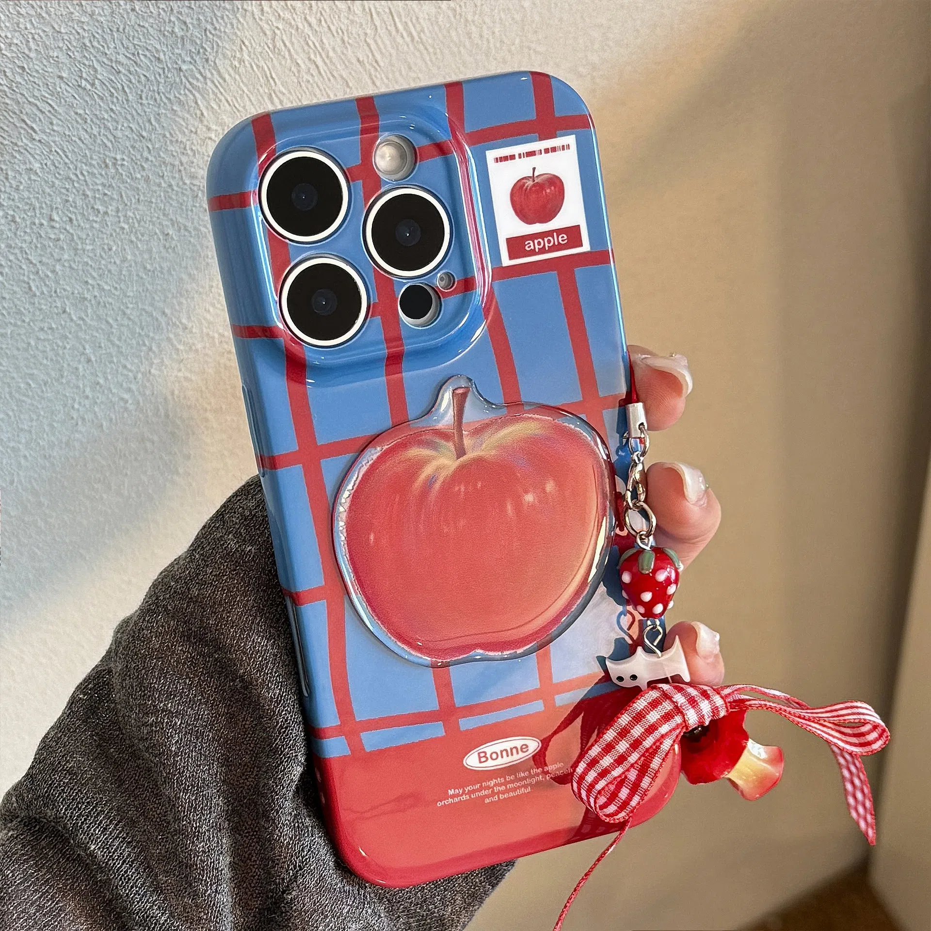 Colour-block checkered 3D fruit phone case for iPhone with blue red grid pattern and red fruit design pendant on a white background