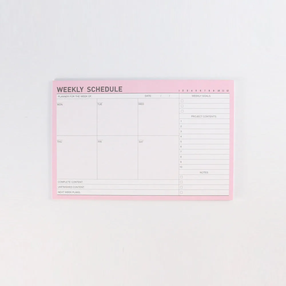 Domikee paper desk organiser pad open showing weekly and monthly planning templates with pink and green cover.