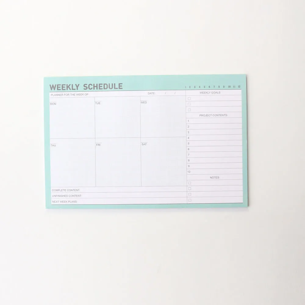 Domikee paper desk organiser pad open showing weekly and monthly planning templates with pink and green cover.