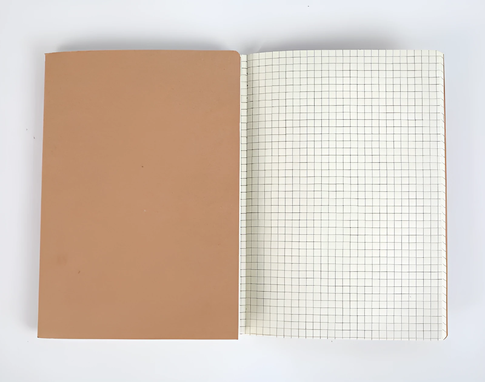 Beige softcover thread-bound notebook in 16K size lying open on a table, showing grid paper inside.