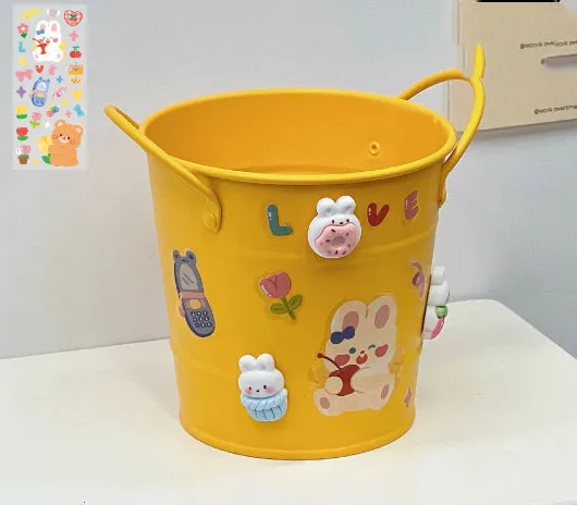 Round metal pen holder in a choice of colours, some with decorative sticker patches, on a wooden desk.
