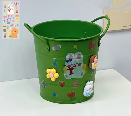 Round metal pen holder in a choice of colours, some with decorative sticker patches, on a wooden desk.