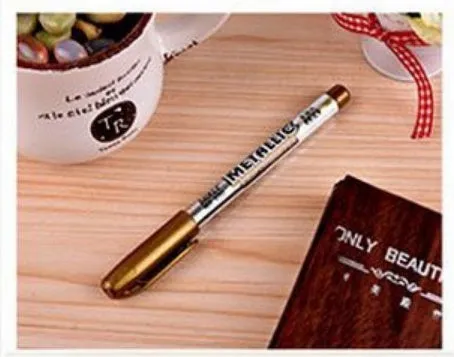 Gold and silver metallic marker pens on a glass surface showing fine tip ink marks