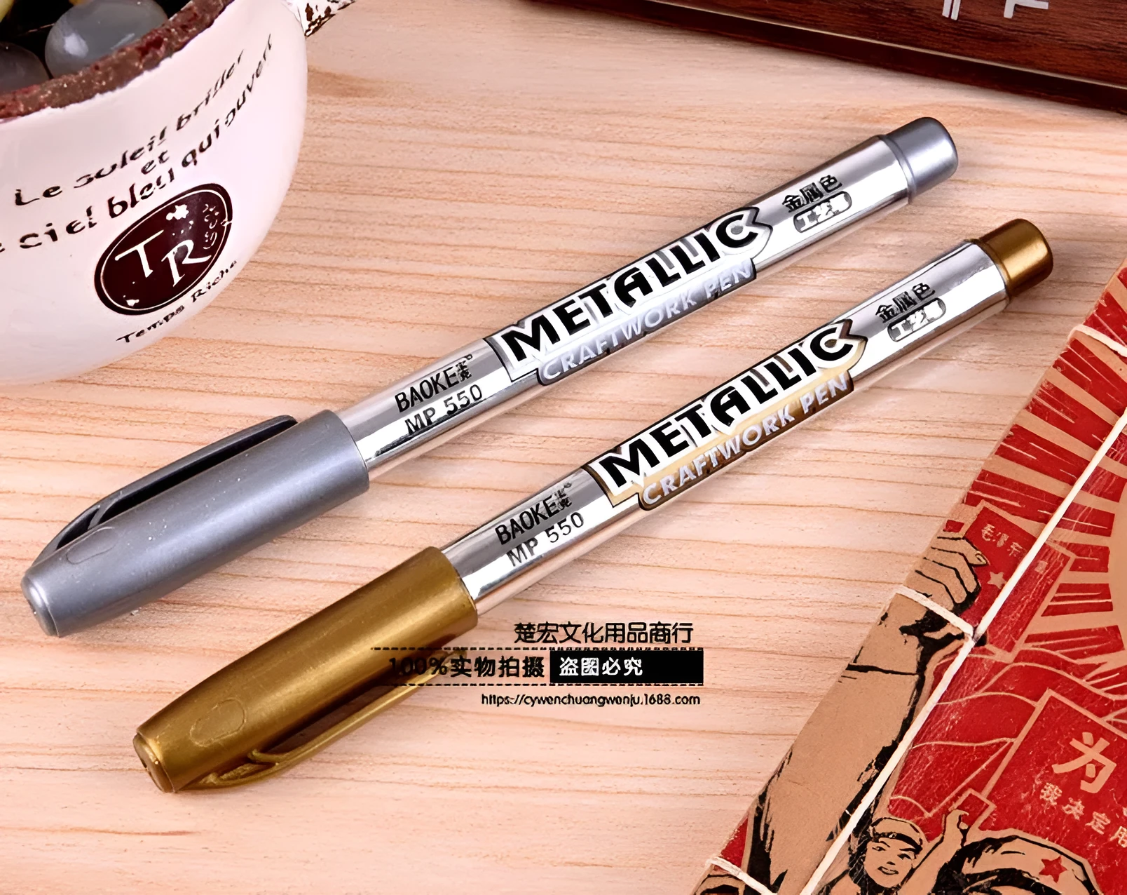 Gold and silver metallic marker pens on a glass surface showing fine tip ink marks