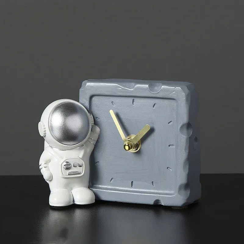 Astronaut resin clock trinket decoration in gold finish on a wooden desk with a bookshelf in background