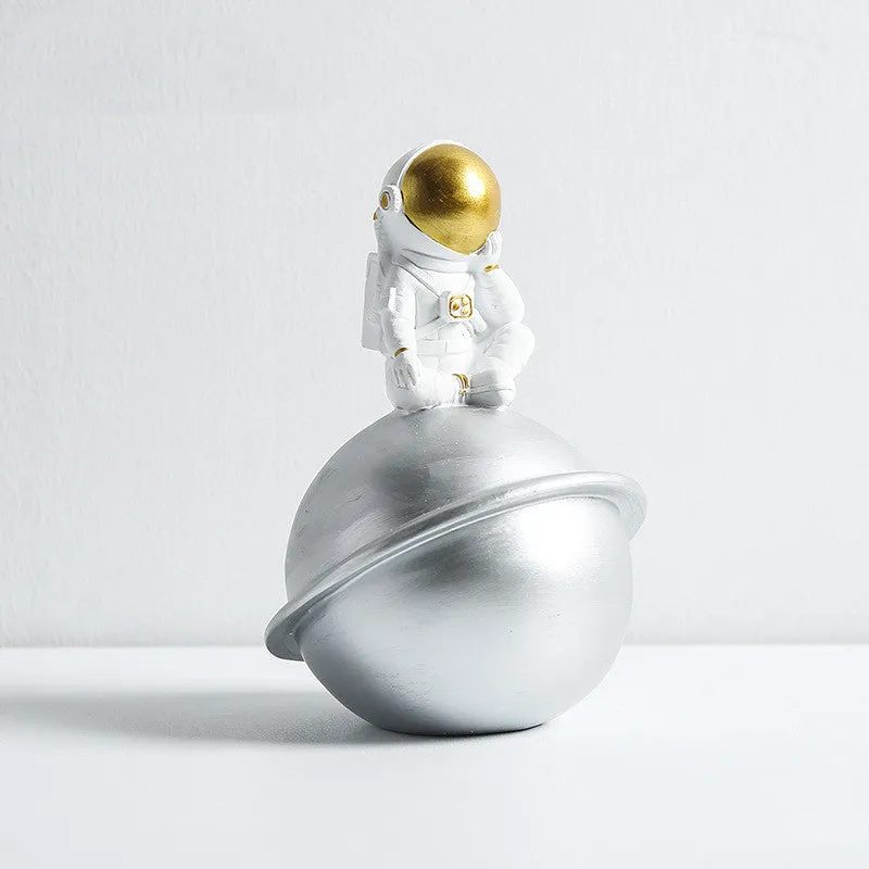 Astronaut resin clock trinket decoration in gold finish on a wooden desk with a bookshelf in background