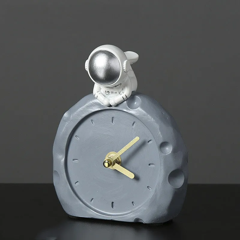 Astronaut resin clock trinket decoration in gold finish on a wooden desk with a bookshelf in background