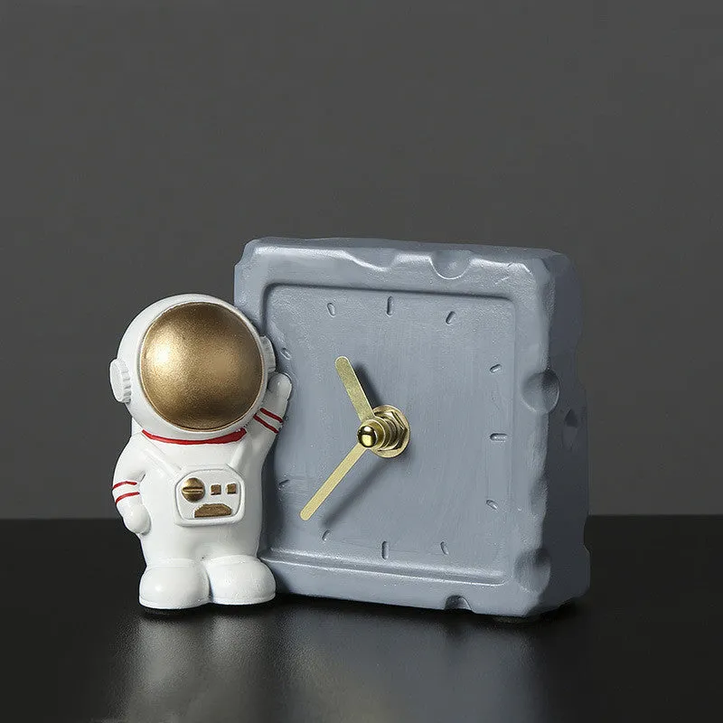 Astronaut resin clock trinket decoration in gold finish on a wooden desk with a bookshelf in background