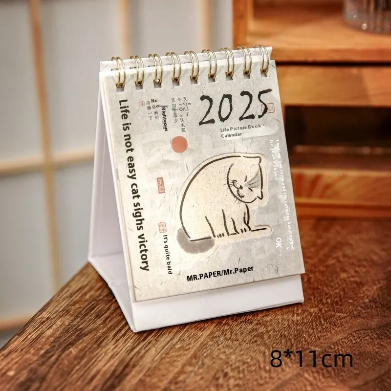 Small 2025 mini desk calendar open to a daily page, showing modern simple design on a desk.