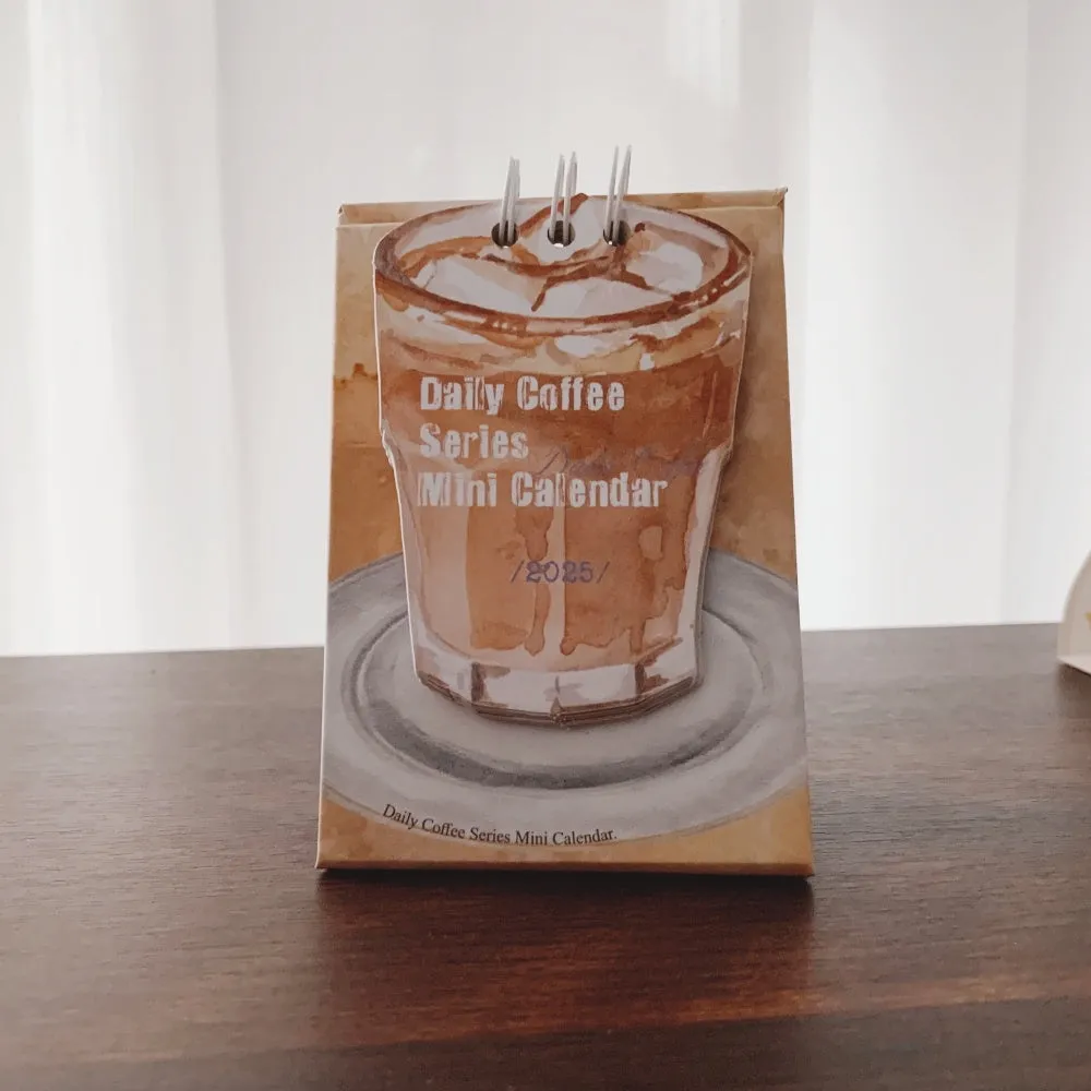 Small 2025 mini desk calendar open to a daily page, showing modern simple design on a desk.