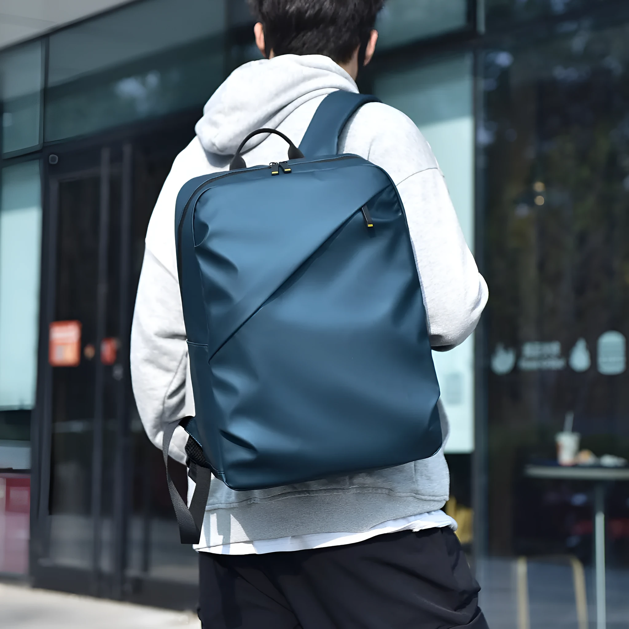 Men's large waterproof black PU leather backpack with laptop compartment on a grey background.