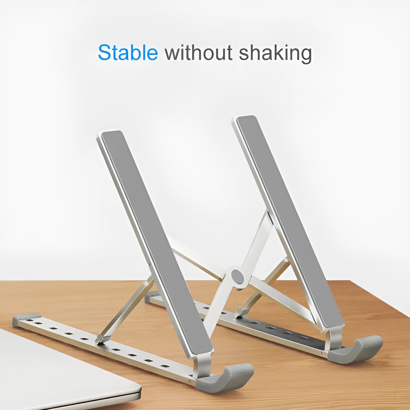 Folding laptop stand in silver with adjustable angle, holding a laptop, showing hollow bottom and non-slip silicone pads