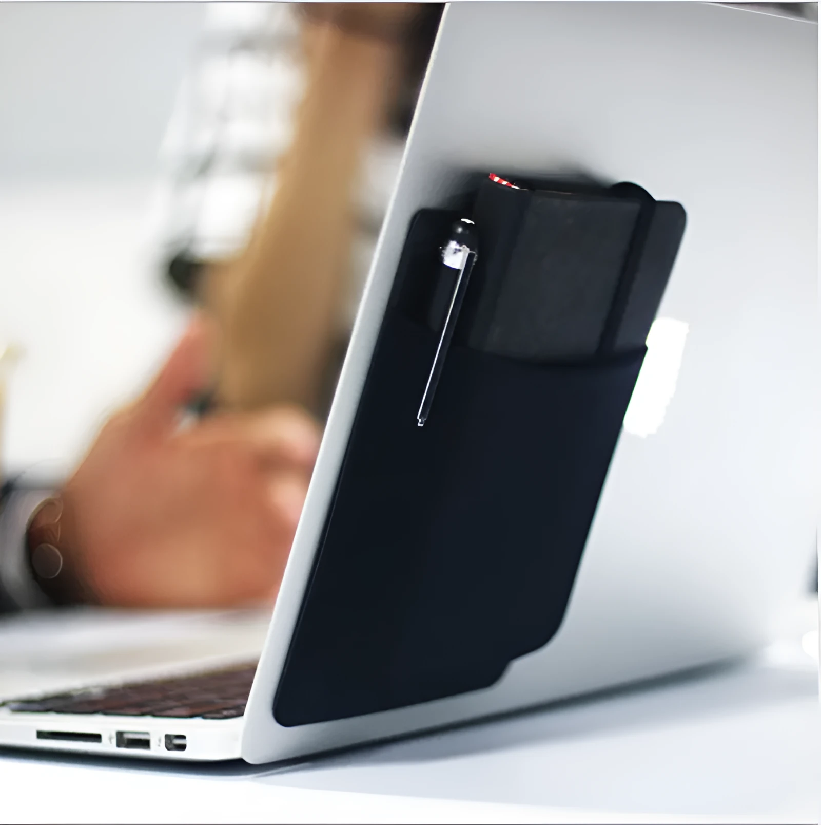 Black adhesive laptop back storage bag attached to a laptop, 15x12 cm, with pen loop and small items inside