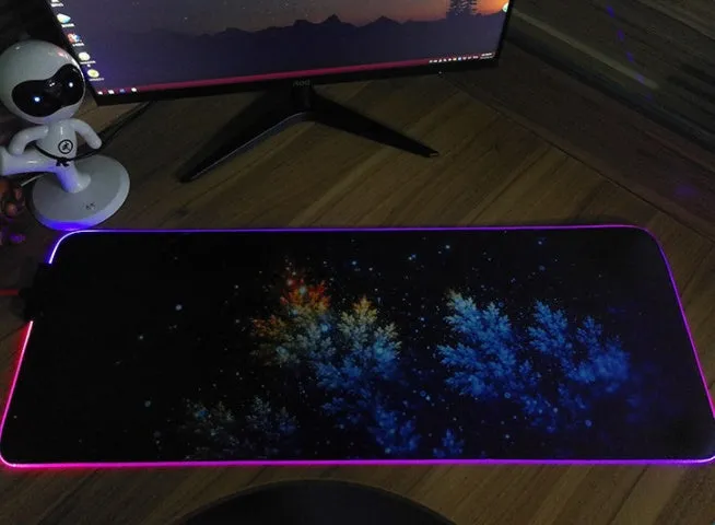 RGB luminous mouse pad with multi-colour LED lighting, fabric surface, and rubber base, shown on a desk with a mouse and keyboard