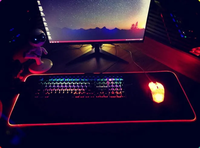 RGB luminous mouse pad with multi-colour LED lighting, fabric surface, and rubber base, shown on a desk with a mouse and keyboard