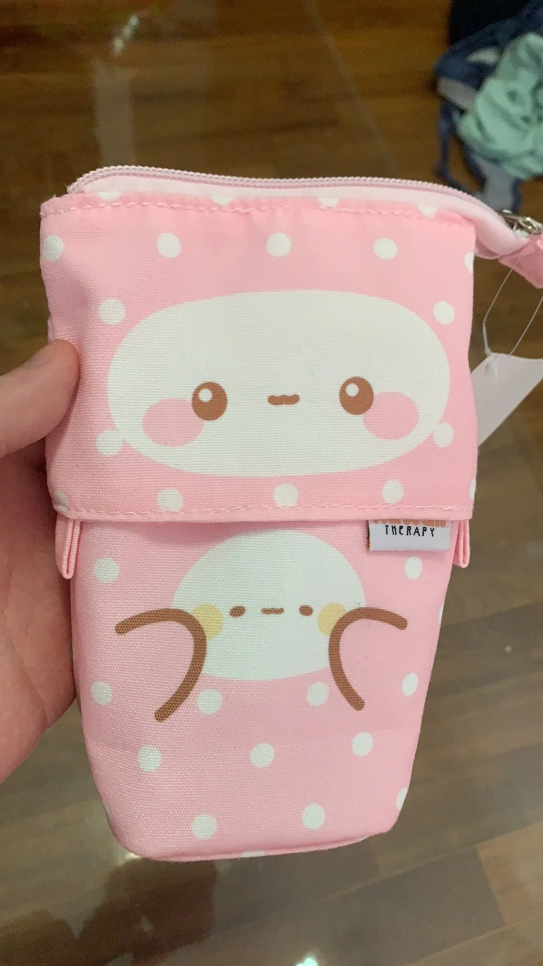 Pink polyester pencil case with zip closure on a desk, surrounded by pens and pencils
