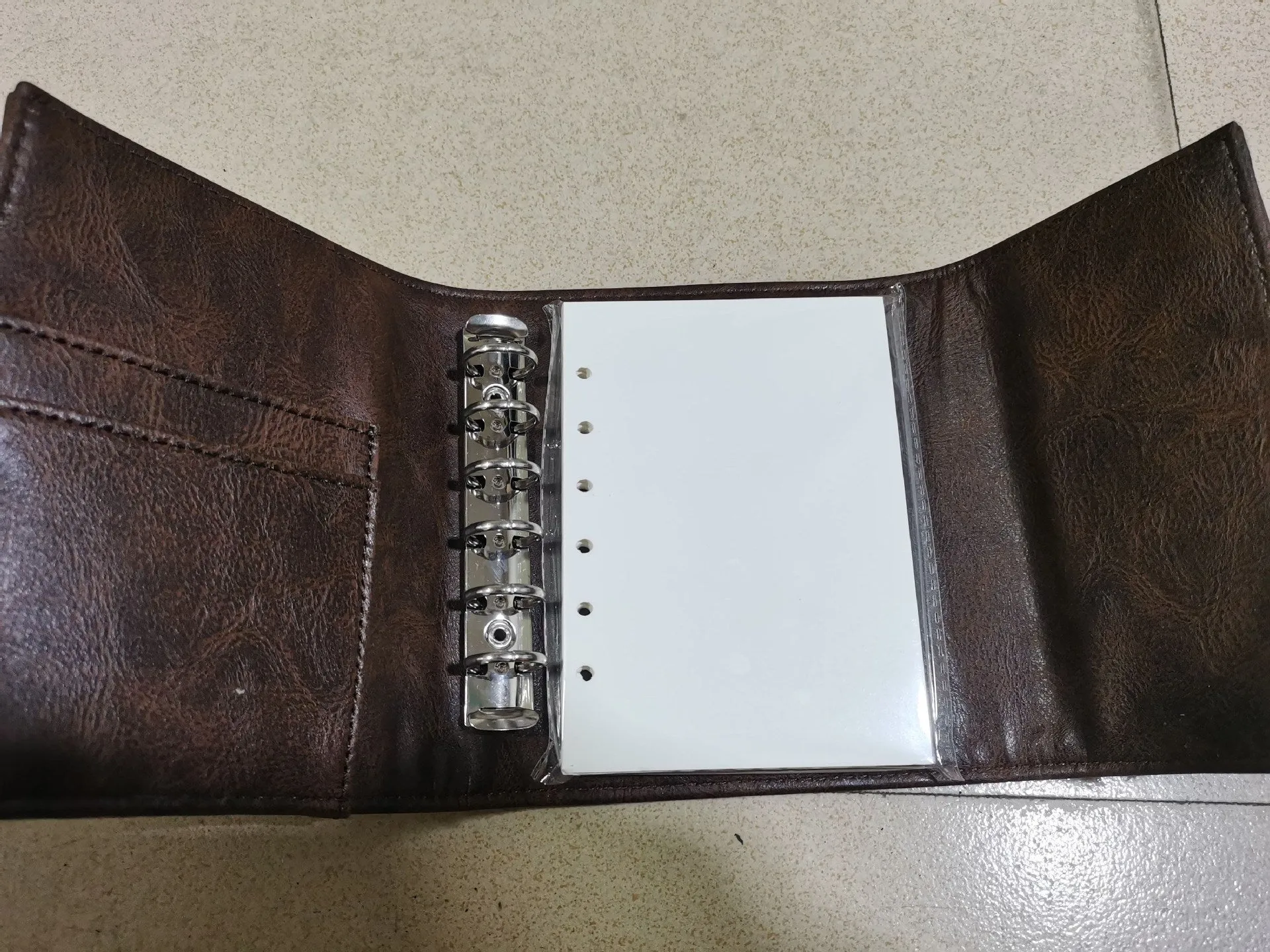 Brown retro-style A7 notebook with a PU leather-look cover and metal buckle closure, showing loose-leaf binding.