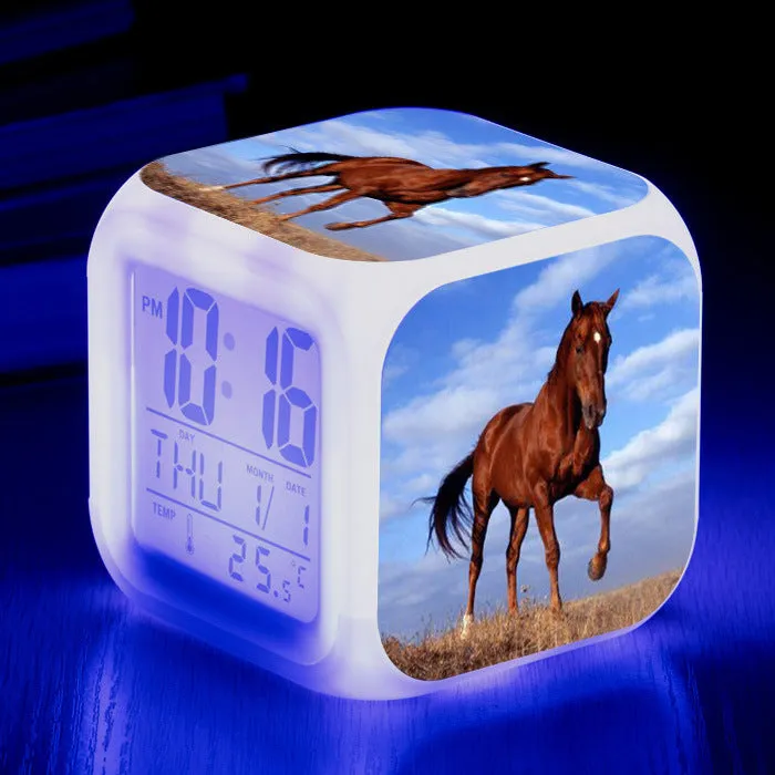 Small square cartoon-style LED alarm clock with colour-changing light feature on a table.