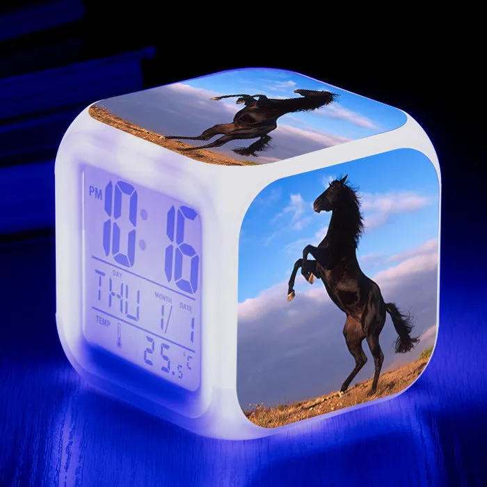 Small square cartoon-style LED alarm clock with colour-changing light feature on a table.