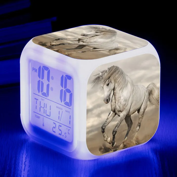 Small square cartoon-style LED alarm clock with colour-changing light feature on a table.