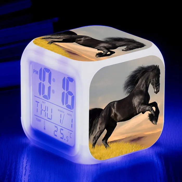 Small square cartoon-style LED alarm clock with colour-changing light feature on a table.