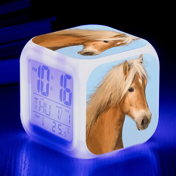 Small square cartoon-style LED alarm clock with colour-changing light feature on a table.