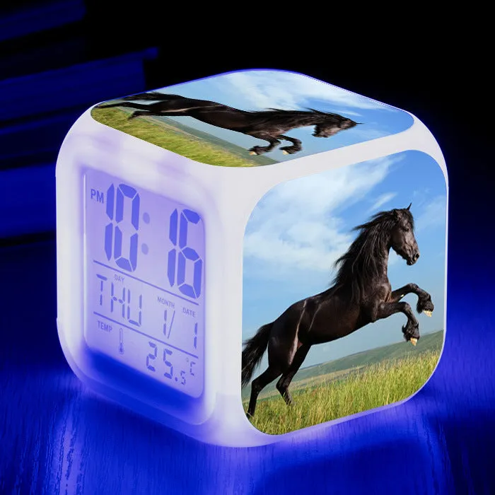 Small square cartoon-style LED alarm clock with colour-changing light feature on a table.
