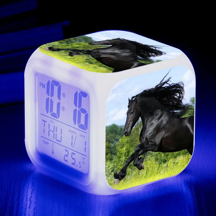 Small square cartoon-style LED alarm clock with colour-changing light feature on a table.