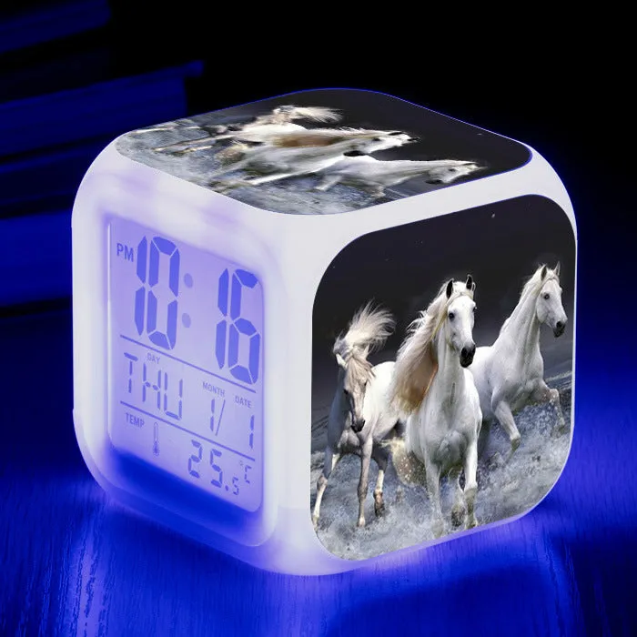 Small square cartoon-style LED alarm clock with colour-changing light feature on a table.