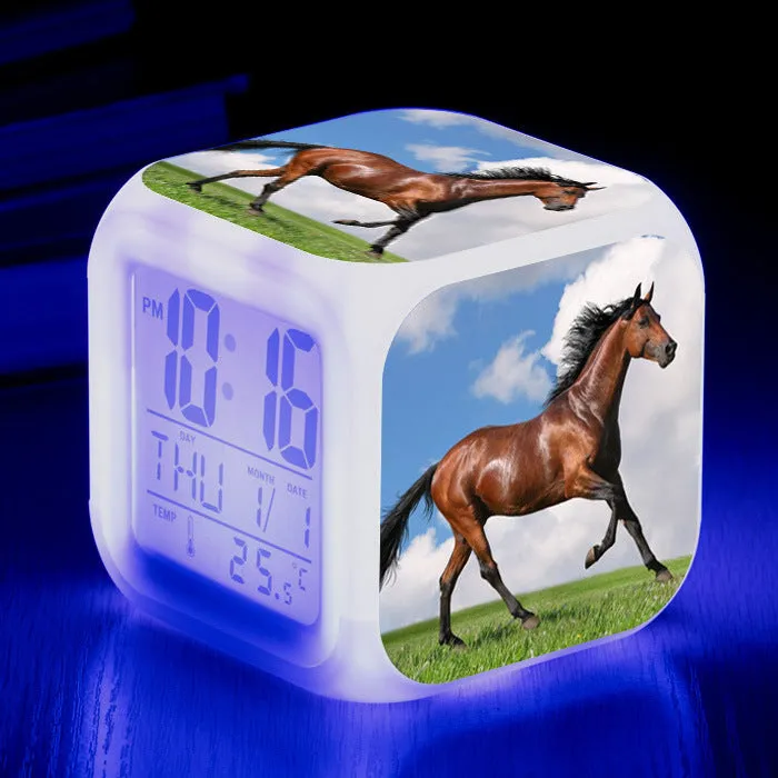 Small square cartoon-style LED alarm clock with colour-changing light feature on a table.