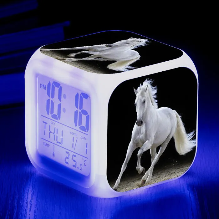 Small square cartoon-style LED alarm clock with colour-changing light feature on a table.