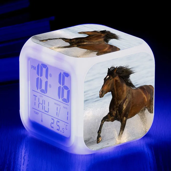 Small square cartoon-style LED alarm clock with colour-changing light feature on a table.