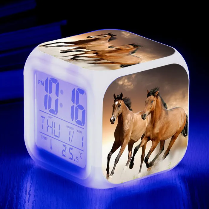 Small square cartoon-style LED alarm clock with colour-changing light feature on a table.