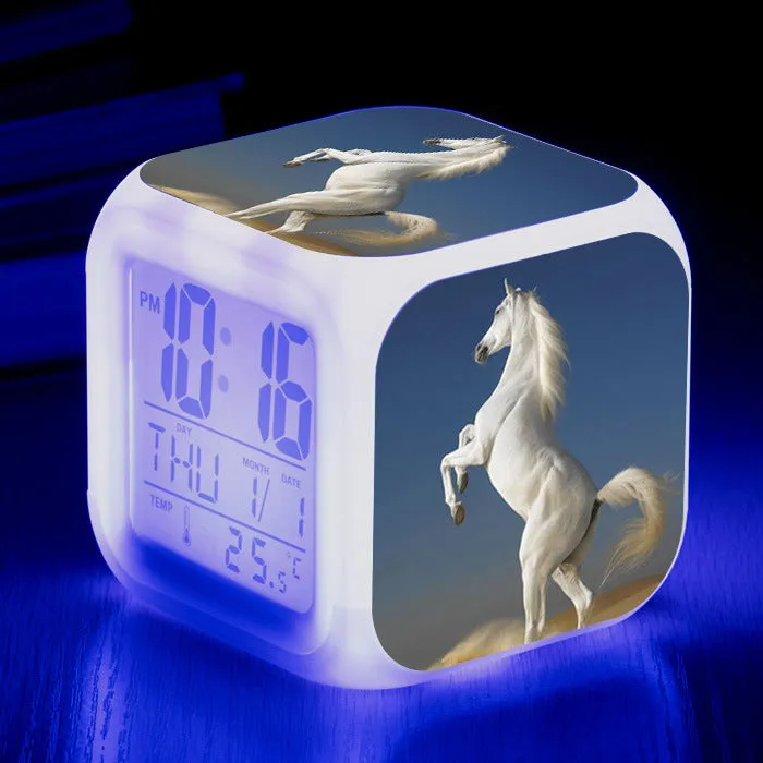 Small square cartoon-style LED alarm clock with colour-changing light feature on a table.