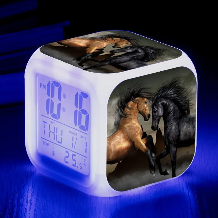 Small square cartoon-style LED alarm clock with colour-changing light feature on a table.