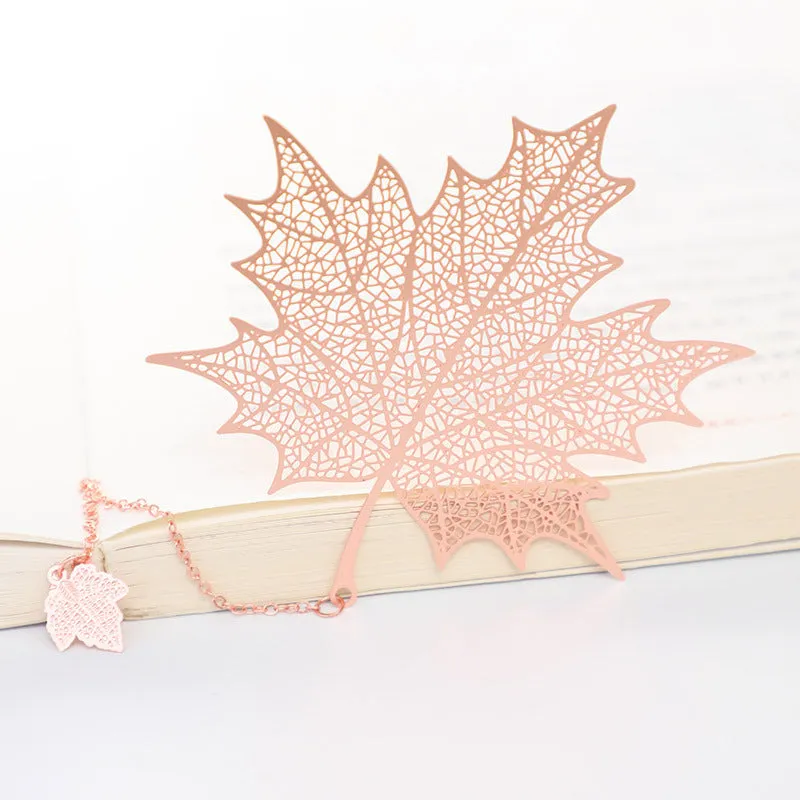 Detailed brass bookmark with hollow maple leaf pendant and rose gold tassel on a book page.