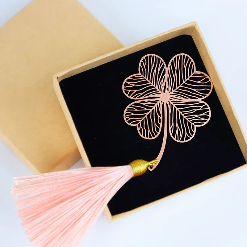 Detailed brass bookmark with hollow maple leaf pendant and rose gold tassel on a book page.