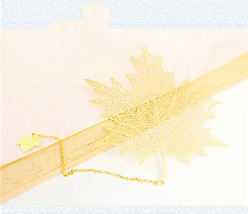 Detailed brass bookmark with hollow maple leaf pendant and rose gold tassel on a book page.
