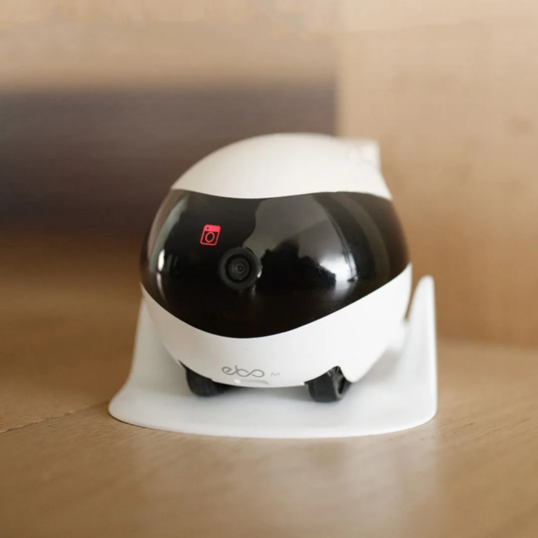 White smart home mobile surveillance robot camera on a docking station.