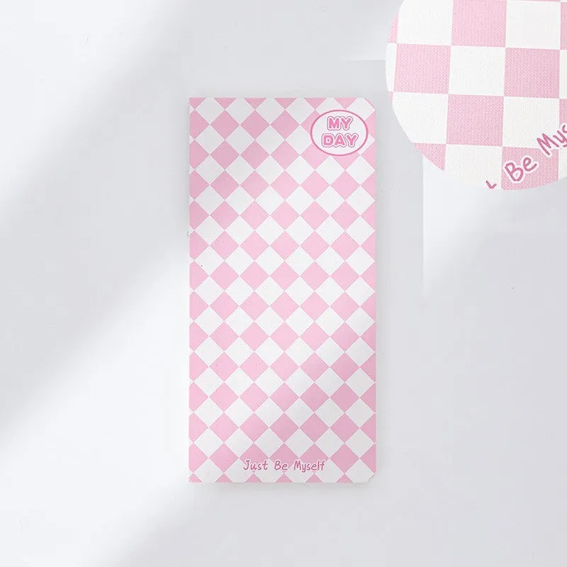 Ins style A5 grid notebook open on a desk, showing grid paper and one of twelve colourful cover designs like pineapple or checkerboard.