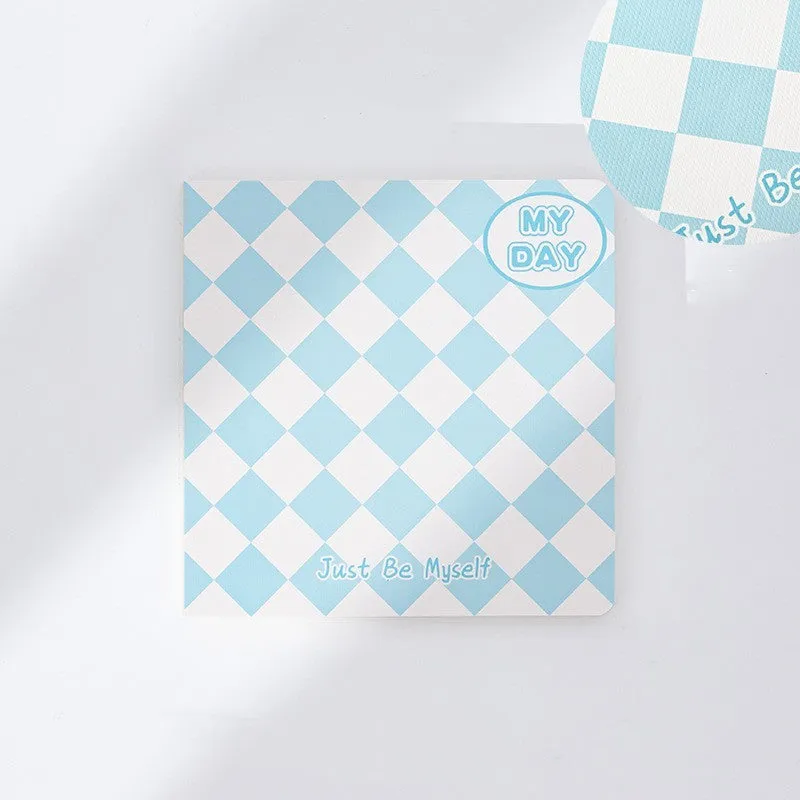 Ins style A5 grid notebook open on a desk, showing grid paper and one of twelve colourful cover designs like pineapple or checkerboard.