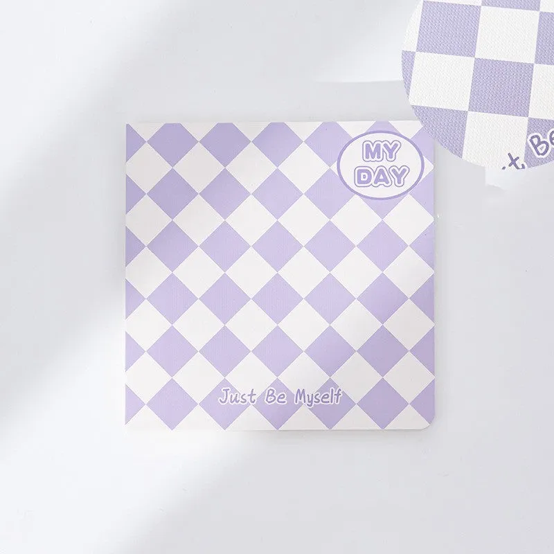 Ins style A5 grid notebook open on a desk, showing grid paper and one of twelve colourful cover designs like pineapple or checkerboard.