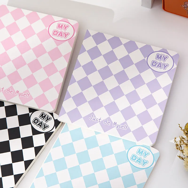 Ins style A5 grid notebook open on a desk, showing grid paper and one of twelve colourful cover designs like pineapple or checkerboard.